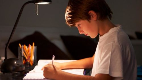 Chico estudiando en su escritorio con una correcta iluminación de flexo y luz neutra
